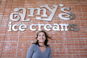 Photo - Amy's Ice Creams founder, Amy, standing in front of a brick wall with the Amy's logo on it.